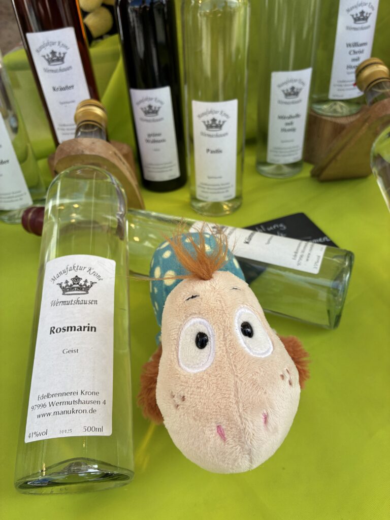 Unterwegs zwischen Aromen Hörschnecke liegt vor verschiedenen Flaschen mit Kräuter- und Spirituosen auf einem Marktstand mit leuchtend grünem Hintergrund.
