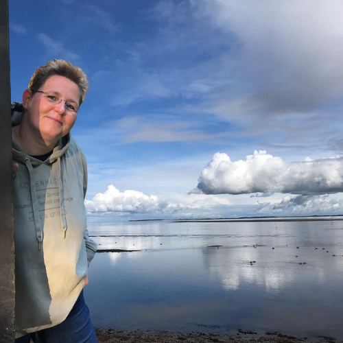 Kerstin Biß steht am Wasser unter weitem Himmel.