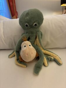 Finnea sitzt zwischen den Armen eines großen Plüsch-Oktopus auf einem Bett.