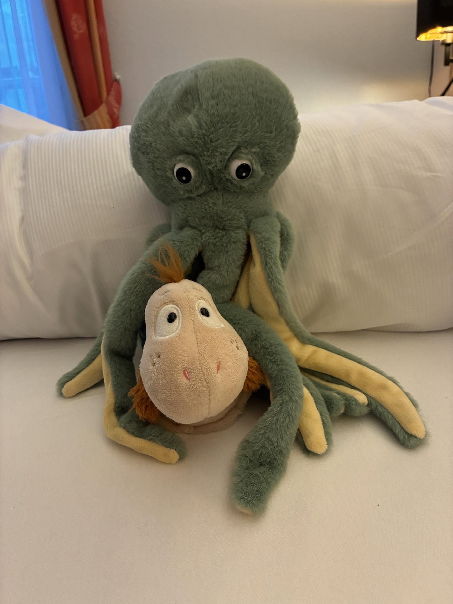 Finnea sitzt zwischen den Armen eines großen Plüsch-Oktopus auf einem Bett.