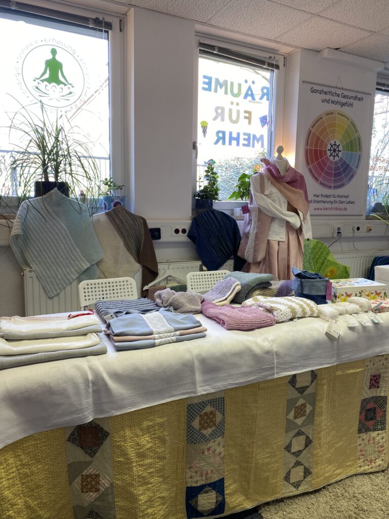 Handgemachtes beim kleinen Markt der Möglichkeiten Gestrickte und genähte Produkte liegen auf einem dekorierten Marktstand.