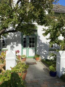 Grün-weiße Haustür an einem weißen Haus, umgeben von Bäumen und Pflanzen.