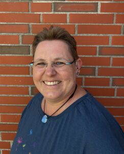 Kerstin Biß lächelt vor einer roten Backsteinwand.